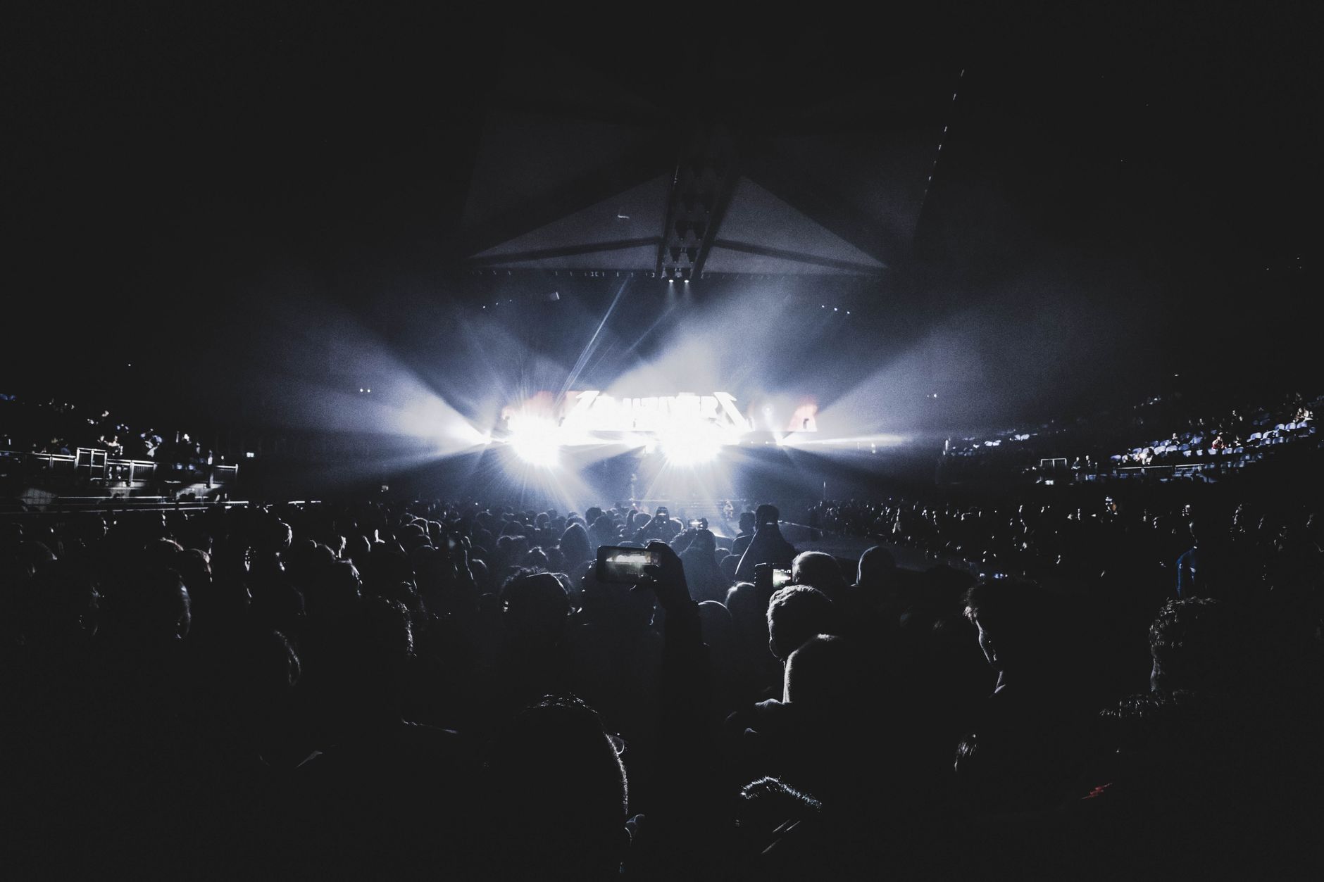 Grote menigte fans met opgestoken handen tijdens een concert in een verlicht stadion