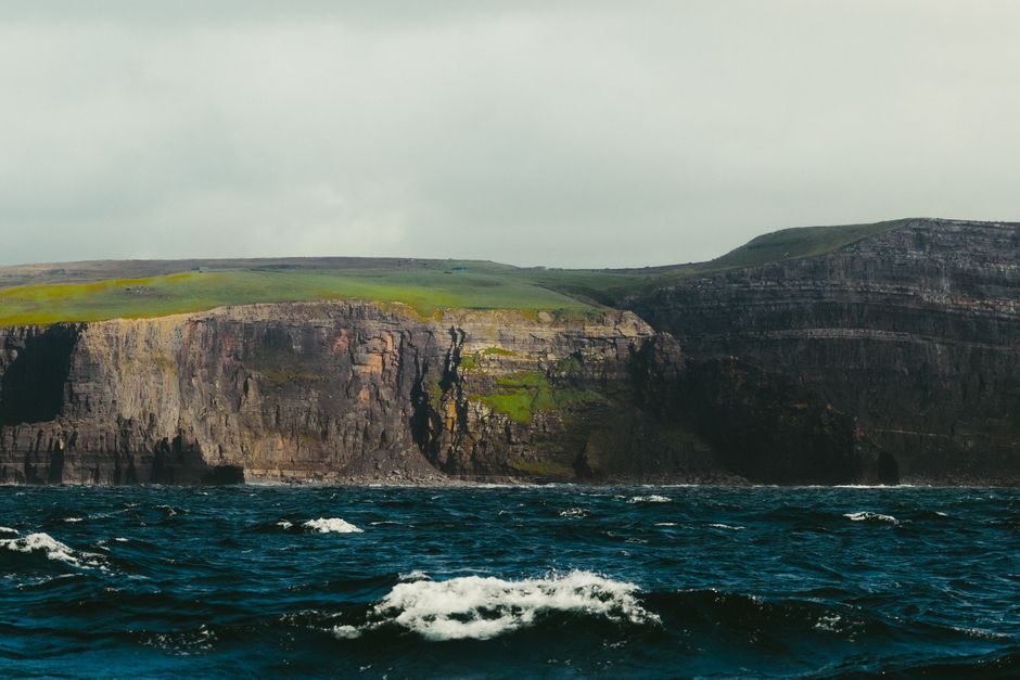 Groene kliffen en kust van Ierland onder een bewolkte lucht, symbool van een reis rond de Ierse Zee